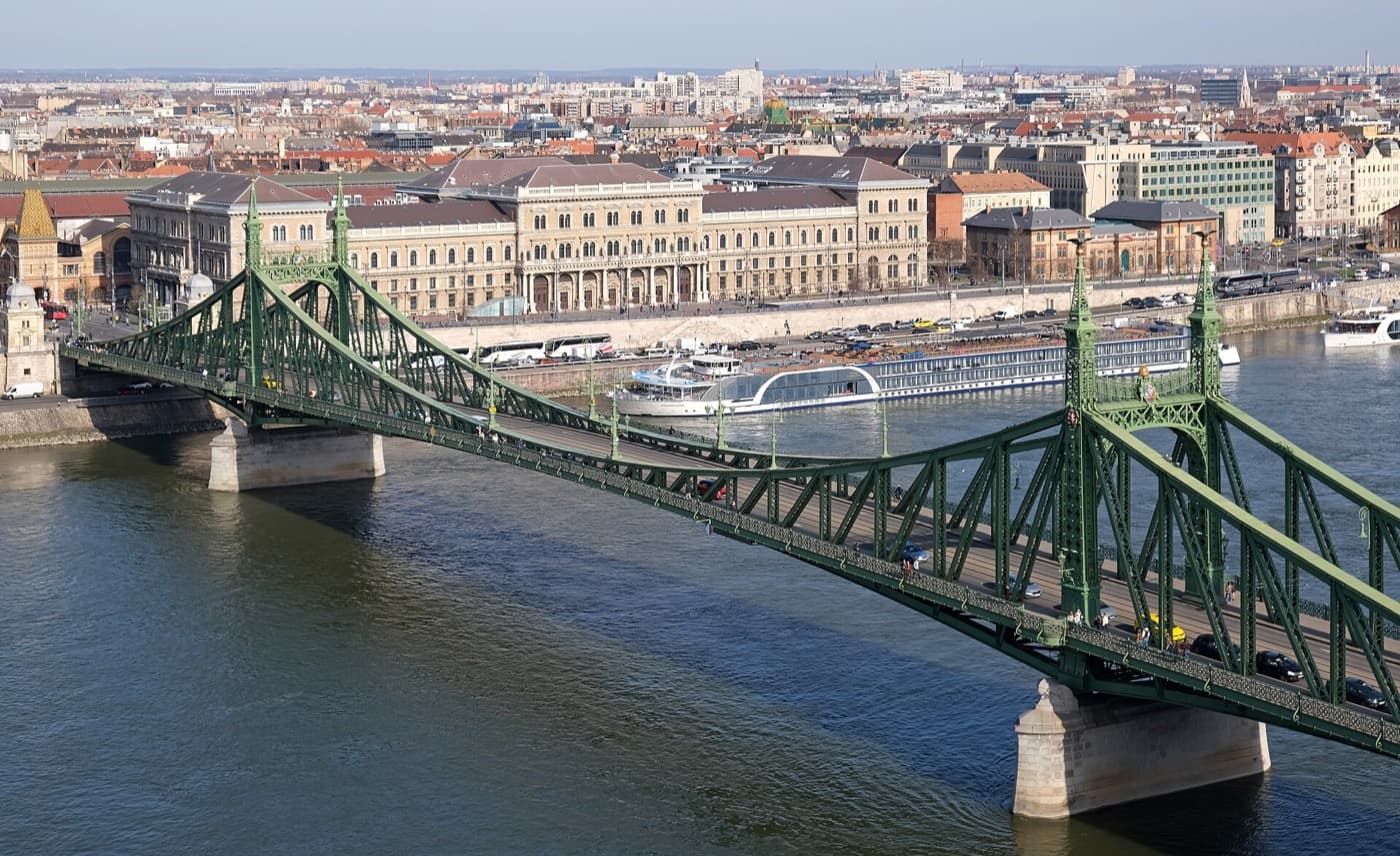 De groene stalen Vrijheidsbrug over de Donau van bovenaf gezien, met aan de Pestse oever het Corvinus-universiteitsgebouw en een rivierboot