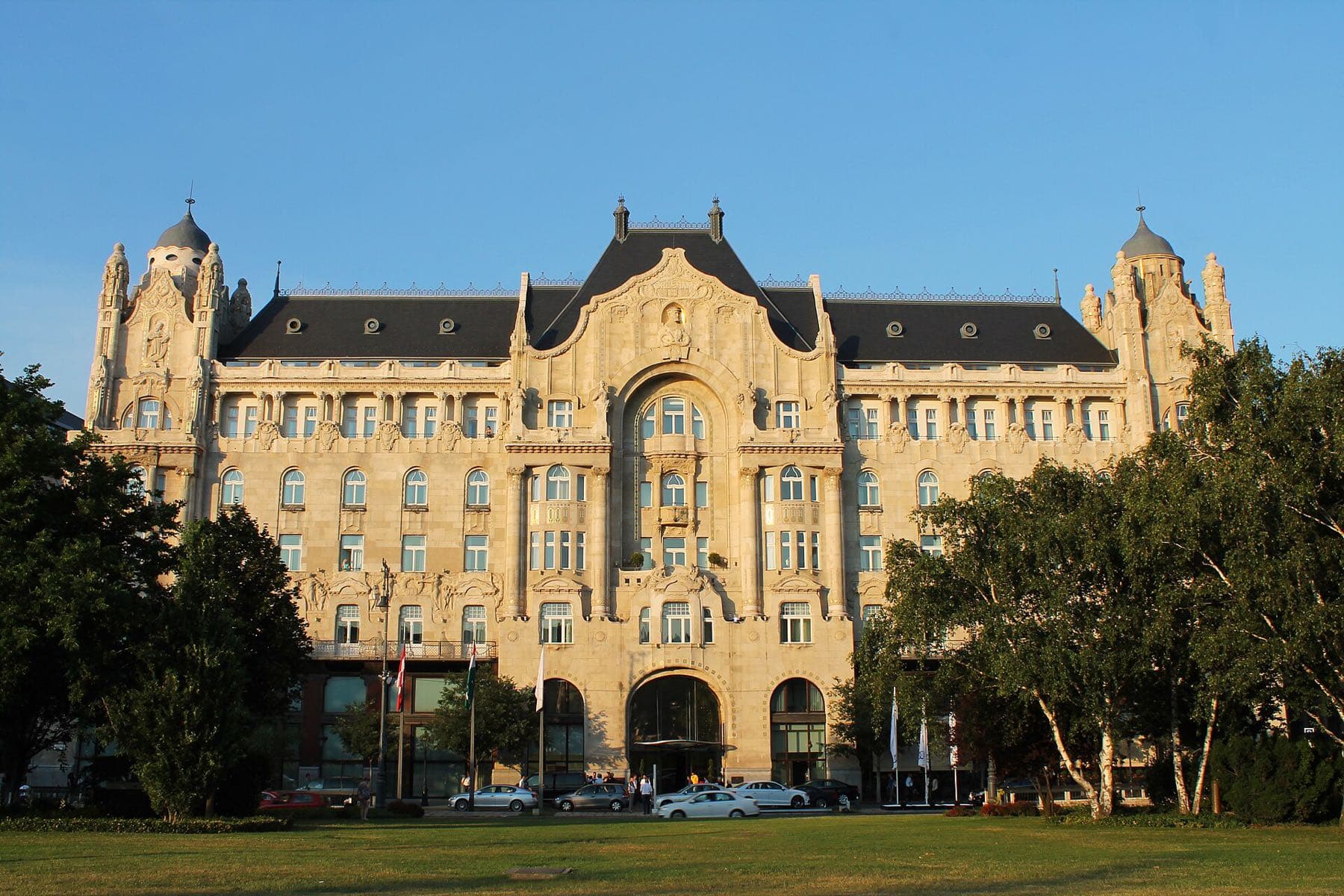Het art-nouveau Greshampaleis (Four Seasons Hotel) aan het Széchenyiplein, met een grasveld en bomen op de voorgrond