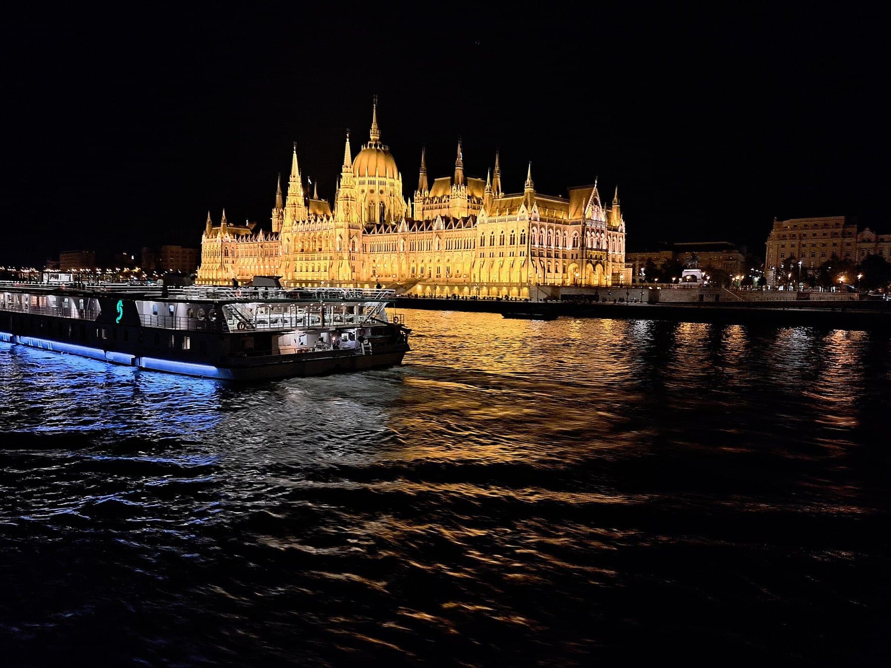 Een verlichte rondvaartboot op de Donau bij nacht, met het goud verlichte Parlementsgebouw op de achtergrond
