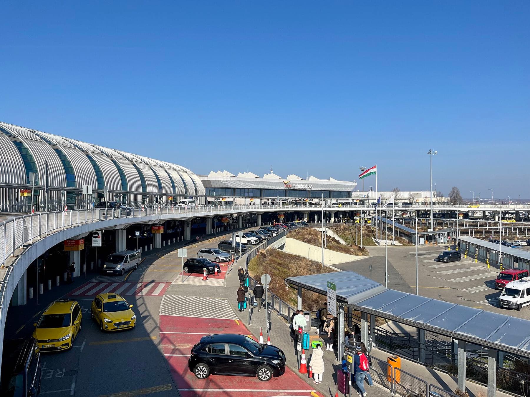 De vertrekhal en oprit van Terminal 2 van Budapest Ferenc Liszt International Airport met gele taxi's en reizigers bij zonnig weer